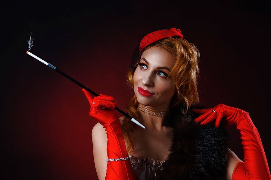 mujer con sombrero y boa negra de plumas. Lleva un bonito traje de estilo burlesque y unos guantes largos de color rojo.