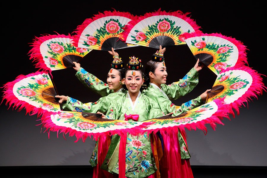 tres chicas asiaticas danzan junto a sus abanicos de color rosa y blanco. Increíble coreografía bailando con estos abanicos grandes para bailar.