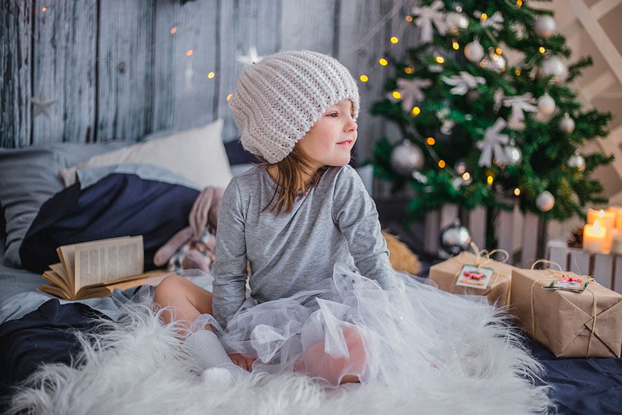 la hija de alguien celebrando la navidad sobre la cama y al lado del arbol navideño. Un arbol navidad boa plumas como decoración.