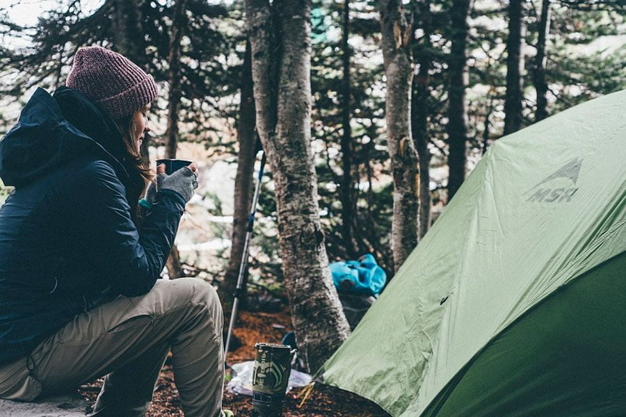 preciosa chica se toma un café en su campamento en mitad del bosque.