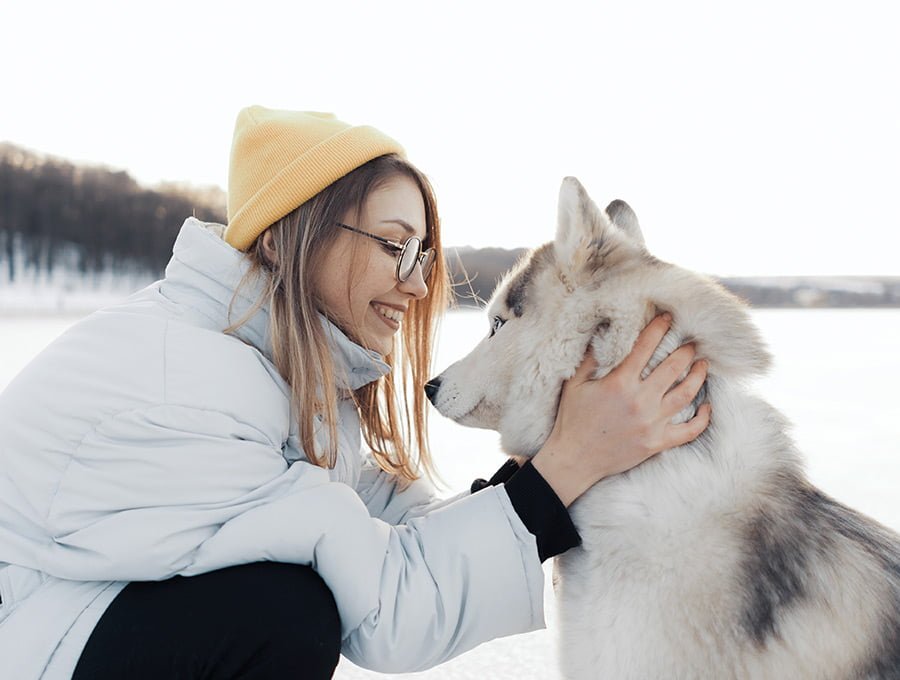 Esta mujer está paseando con su perro por la montaña. Lleva puesto un anorak de pluma para montaña. El perro es un husky siberiano y no tiene nada de frío.