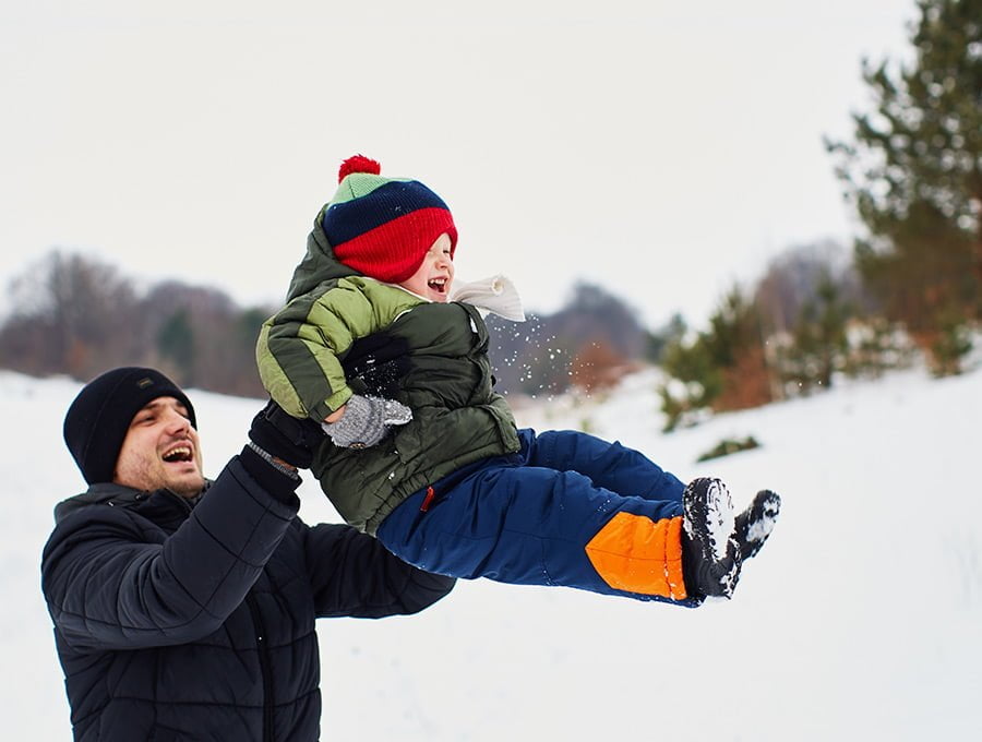 Este padre juega con su hijo a lanzarlo por los aires. Menos mal que si se cae en la nieve no le pasa nada porque está bien abrigado con esa chaqueta verde de plumón.